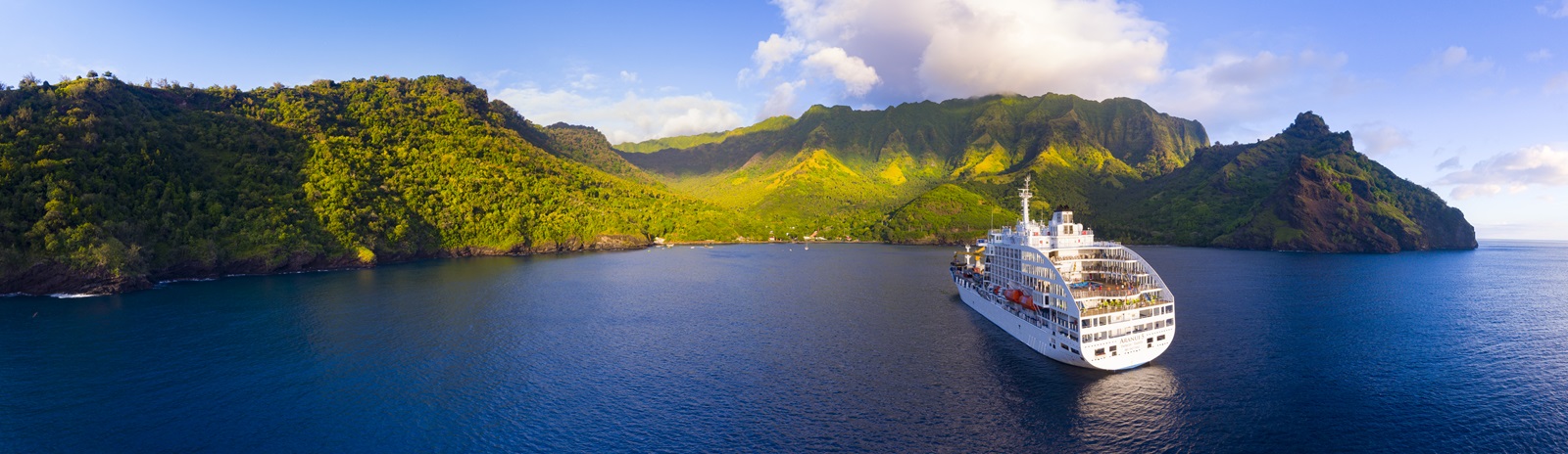 L'ARANUI 5 , paquebot de croisière, arrivant à Tahuata en Polynésie française, avec des montagnes verdoyantes en arrière-plan et des eaux calmes autour.